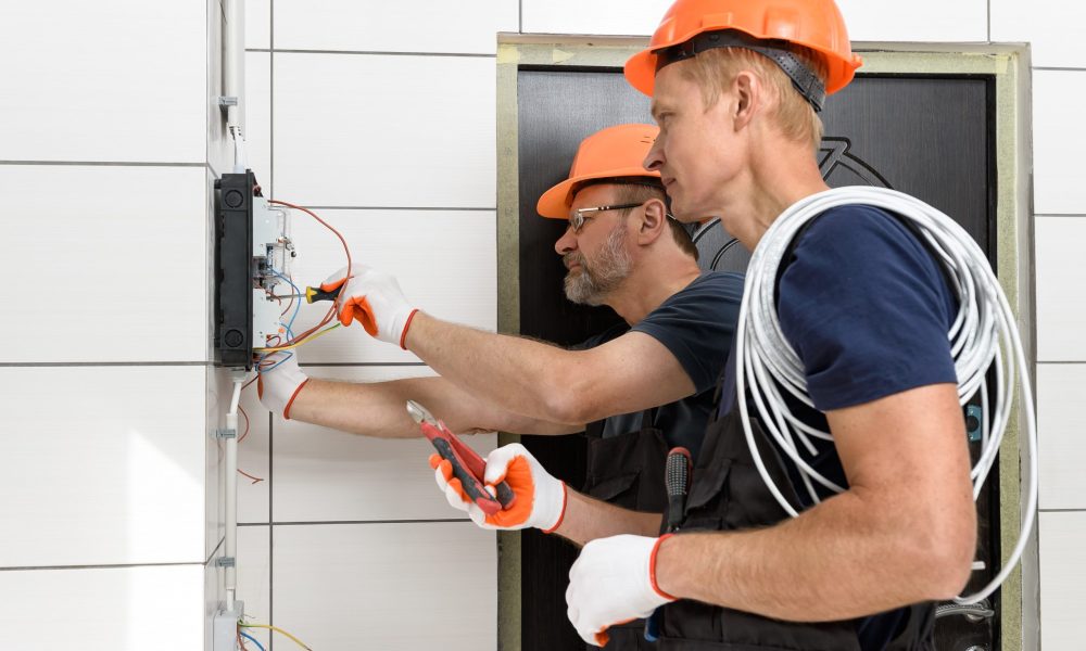 Electricians are installing out wall wiring. They are connecting wires in the junction box.